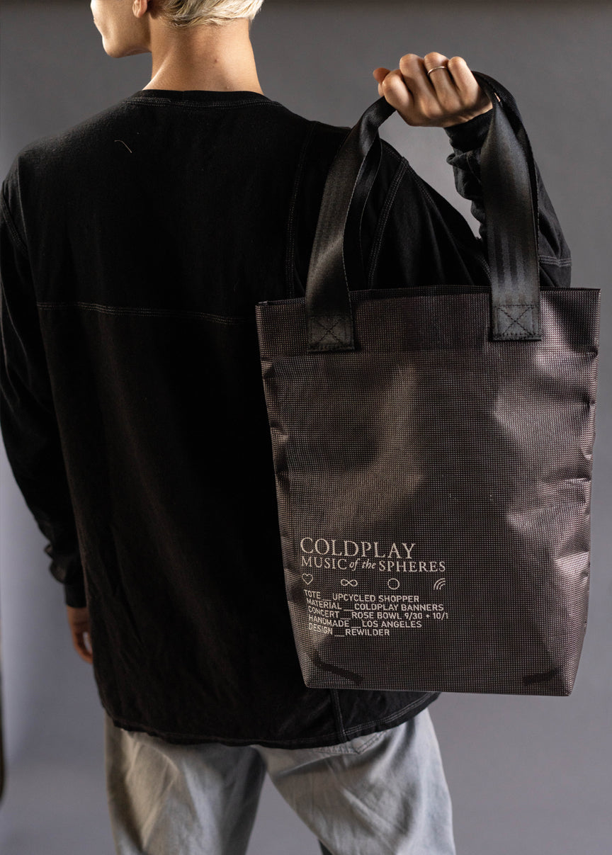Black tote bag made of dark spaces from show posters. In white, COLDPLAY MUSIC OF THE SPHERES. A heart, an infinity sign and Chris’s rainbow doodle. Tote Upcycled Shopper. Material: Coldplay Banners. Concert: Rose Bowl. 9/30 & 10/1. Handmade. Los Angeles. Design: Rewilder. Same as the photo above