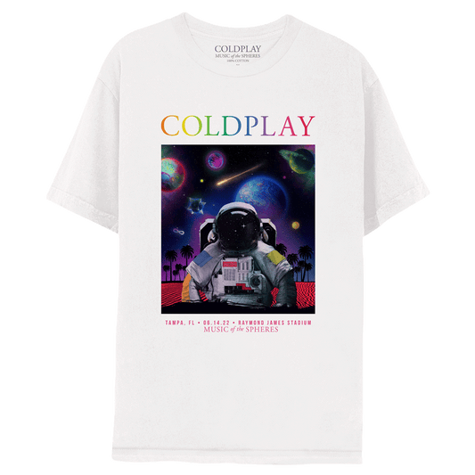 On the front of a white T-shirt is a👨🚀wearing a space suit. He stands surrounded by a serene, red sandy beach of Tampa Bay. Lots of palm tree silhouettes line the horizon. The night sky, filled with stars, is purple, fading to blue, and then to black. Most of the spheres’ planets are present, as well as a shooting star. COLDPLAY is written in neon rainbow colors at the top of the shirt. At the bottom, pink text reads: TAMPA, FL. 06.14.22. RAYMOND JAMES STADIUM. MUSIC OF THE SPHERES.