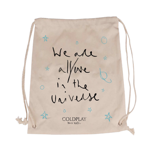 We are all/one in the Universe in Chris’ handwriting on the front of a hemp bag with light blue hand drawn stars, circles, and planets surrounding the text. Coldplay logo and handwritten Moon Music are smaller, centered at the bottom in black.